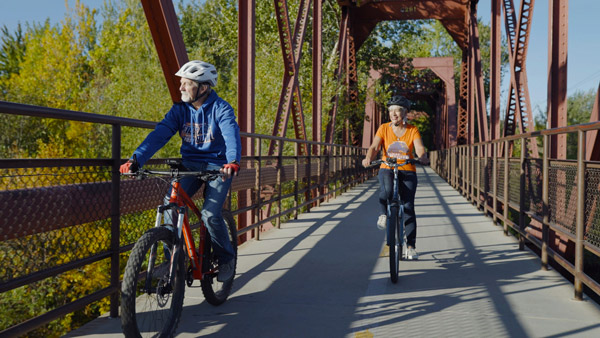 Outdoor photo of senior couple riding their bikes over a bridge